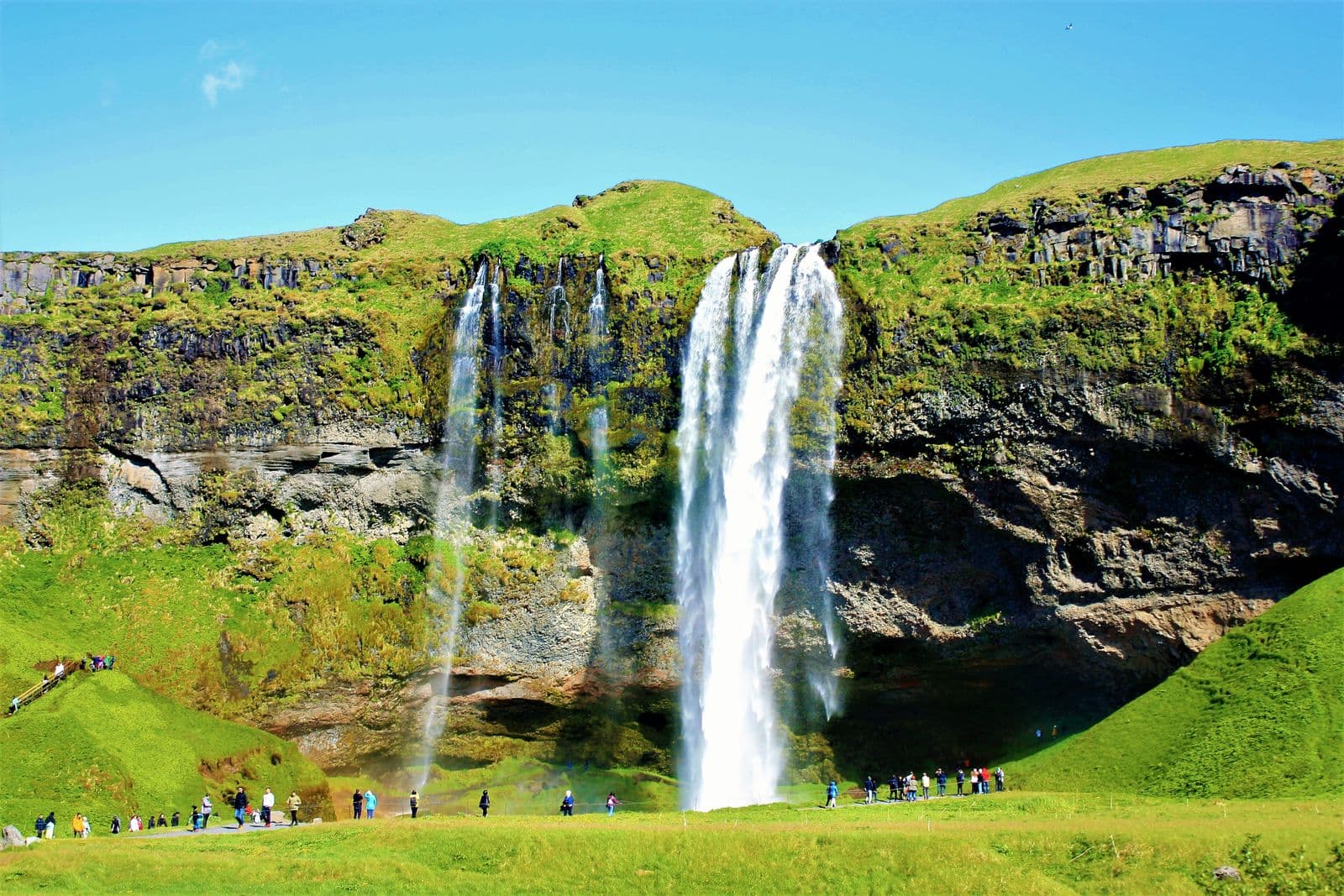 Seljalandsfoss waterfall under a blue sky with visitors walking along the path