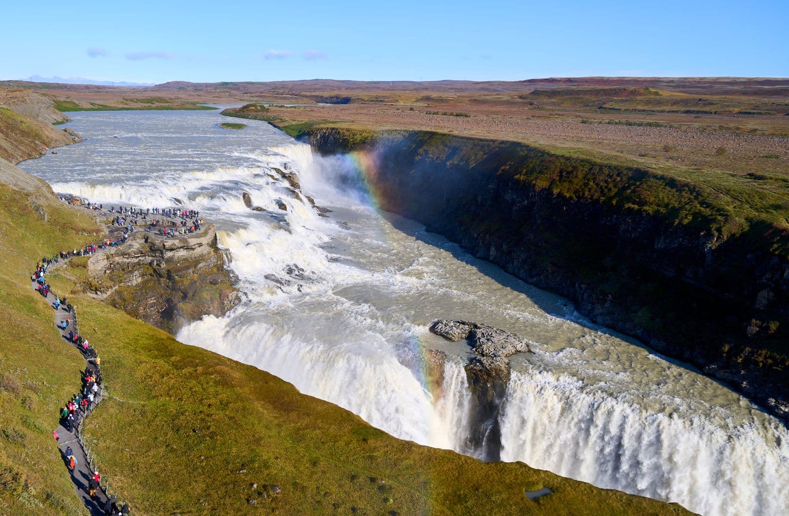 Aerial view of Gullfoss waterfall with a rainbow and a path winding along the canyon edge
