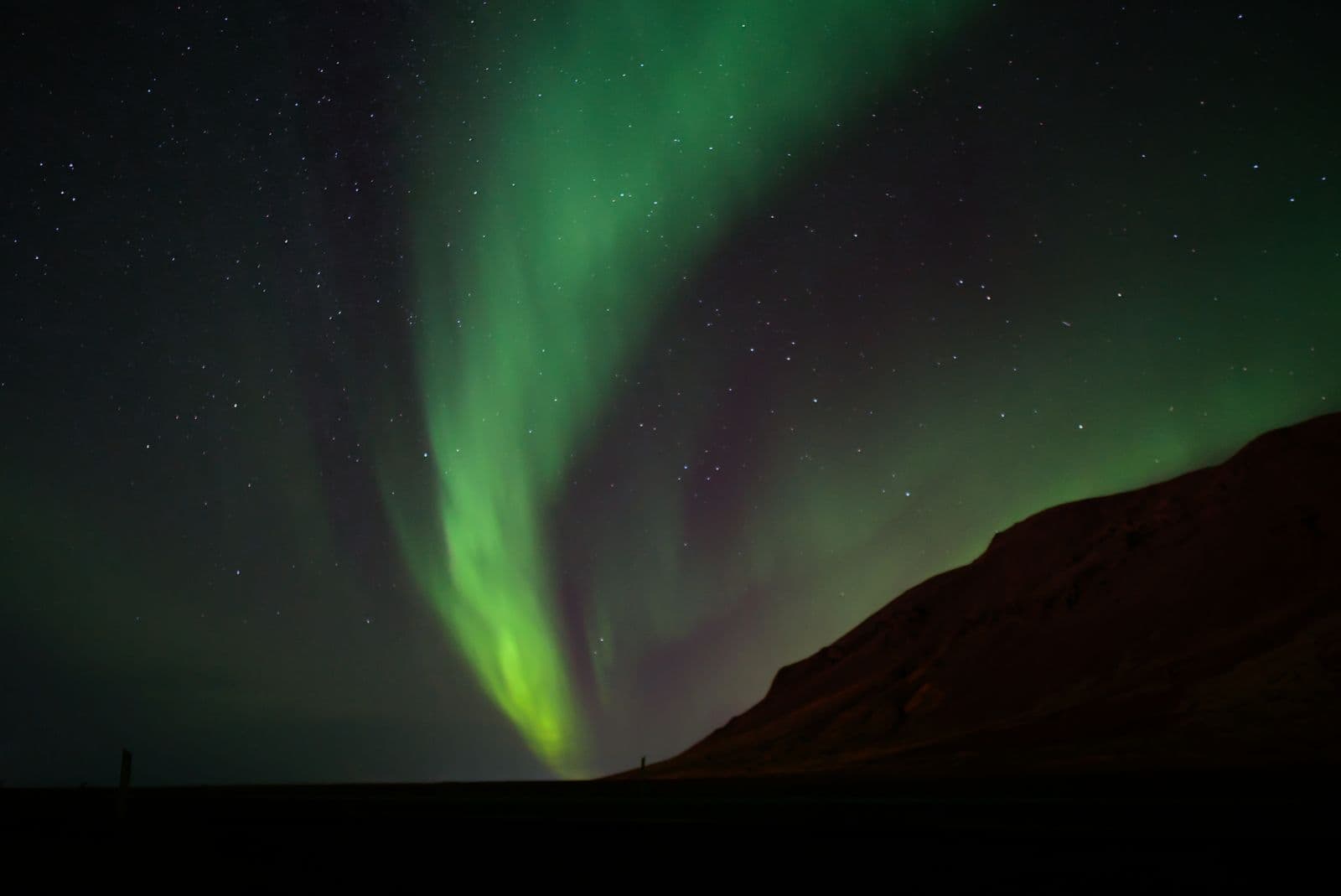 Soft green aurora arcing over a dark mountain slope under a star-filled sky