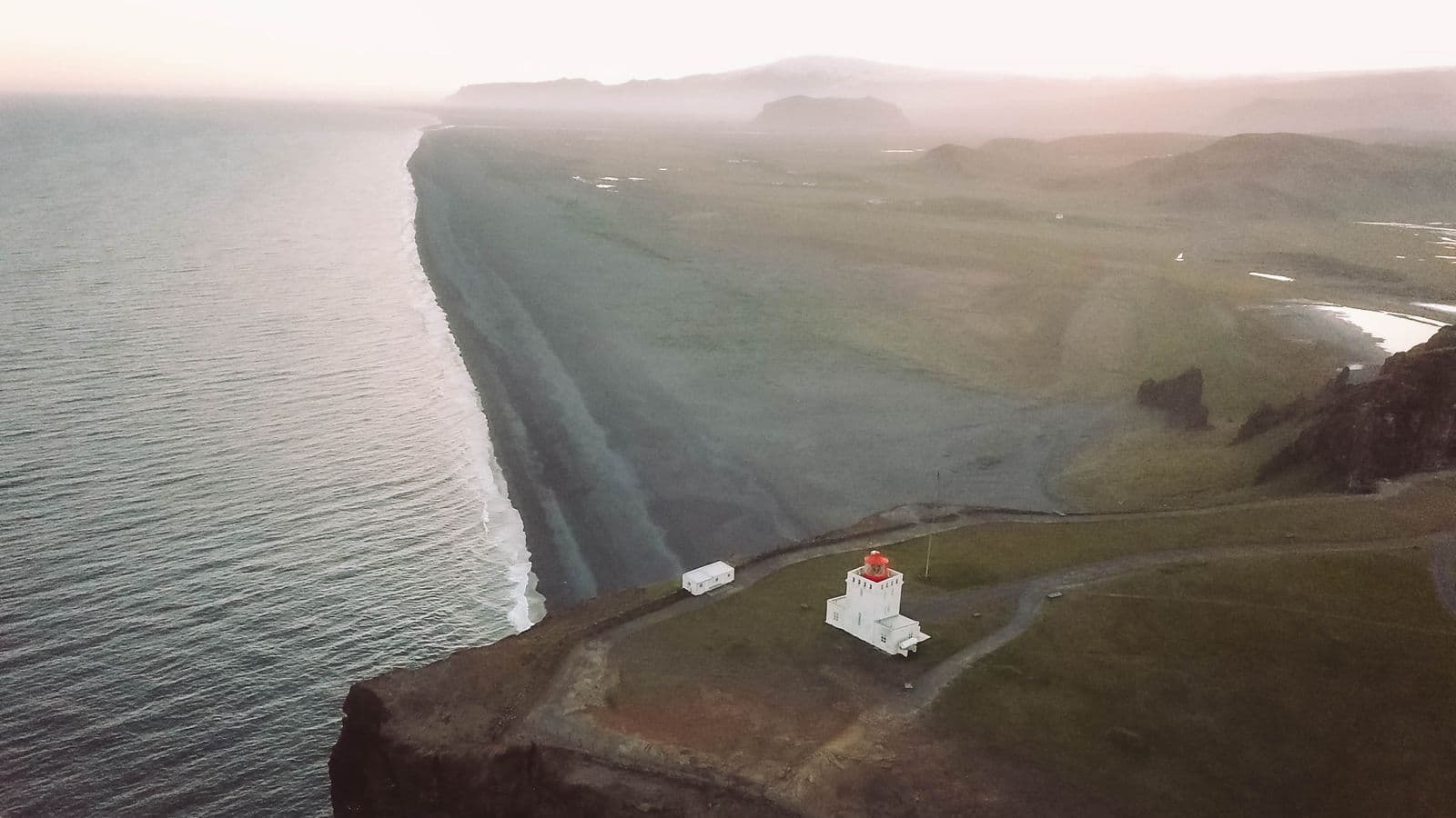 Aerial view of the Dyrhólaey lighthouse on a cliff above a long black sand beach on Iceland's South Coast