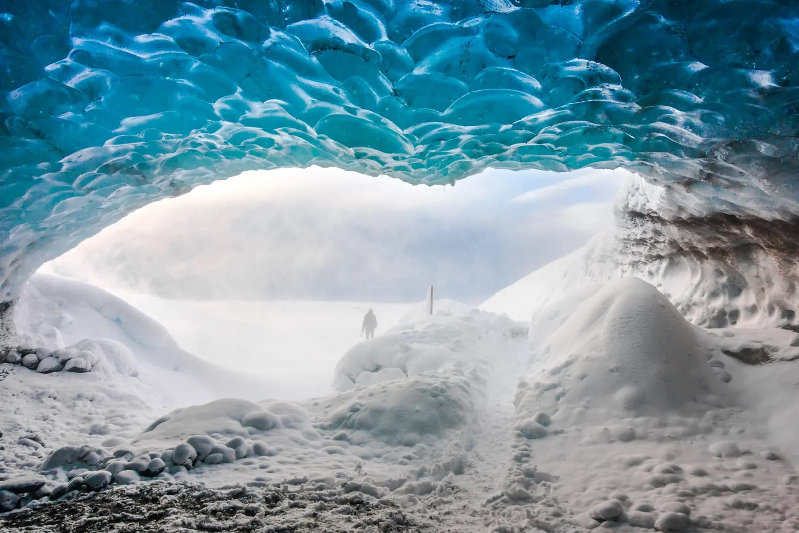 An opening of an ice cave in Vatnajökull glacier with snow and blue ice walls