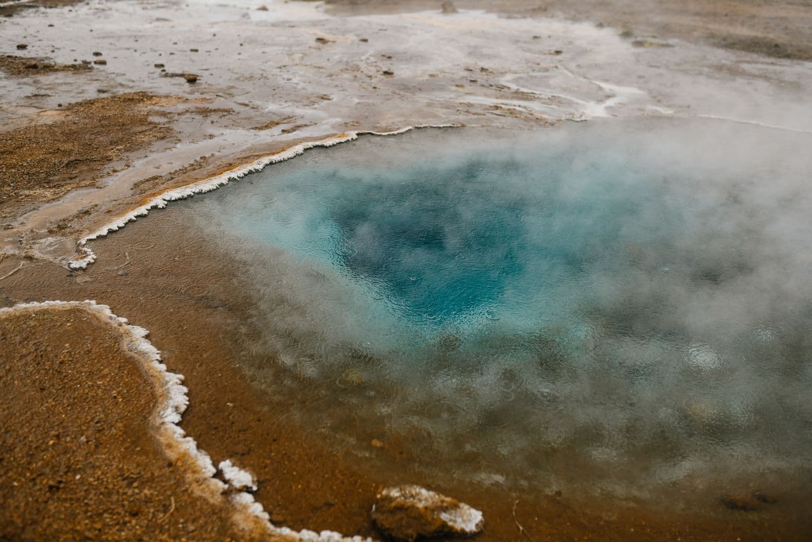 Steaming turquoise hot spring surrounded by mineral crust in an Icelandic geothermal area