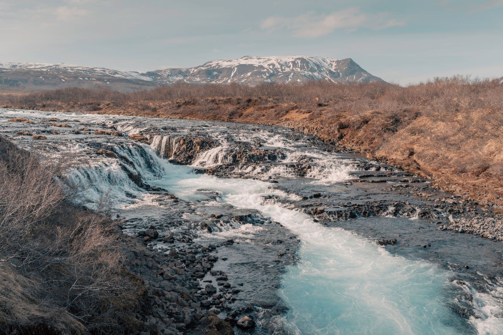 Turquoise river rushing over rocks with snow-capped mountains behind in spring