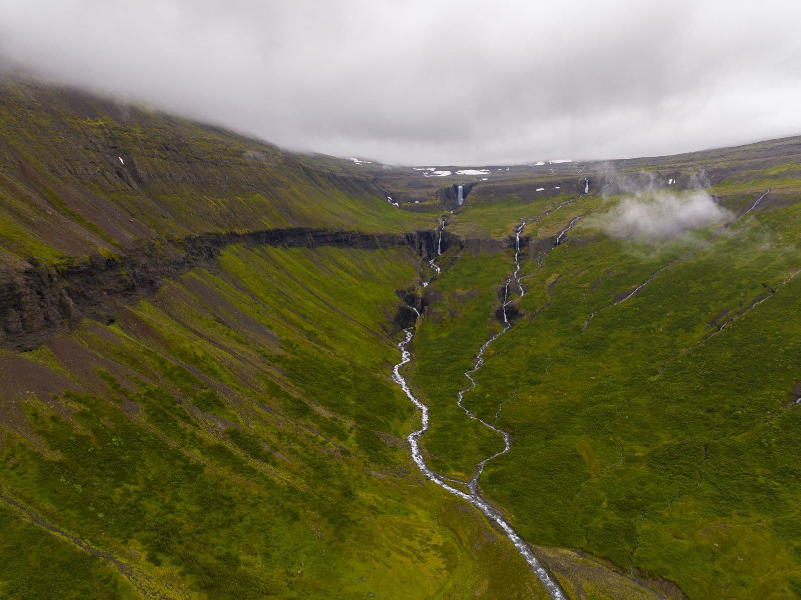 Aerial view of a green Icelandic valley with several waterfalls running down the slopes under low cloud