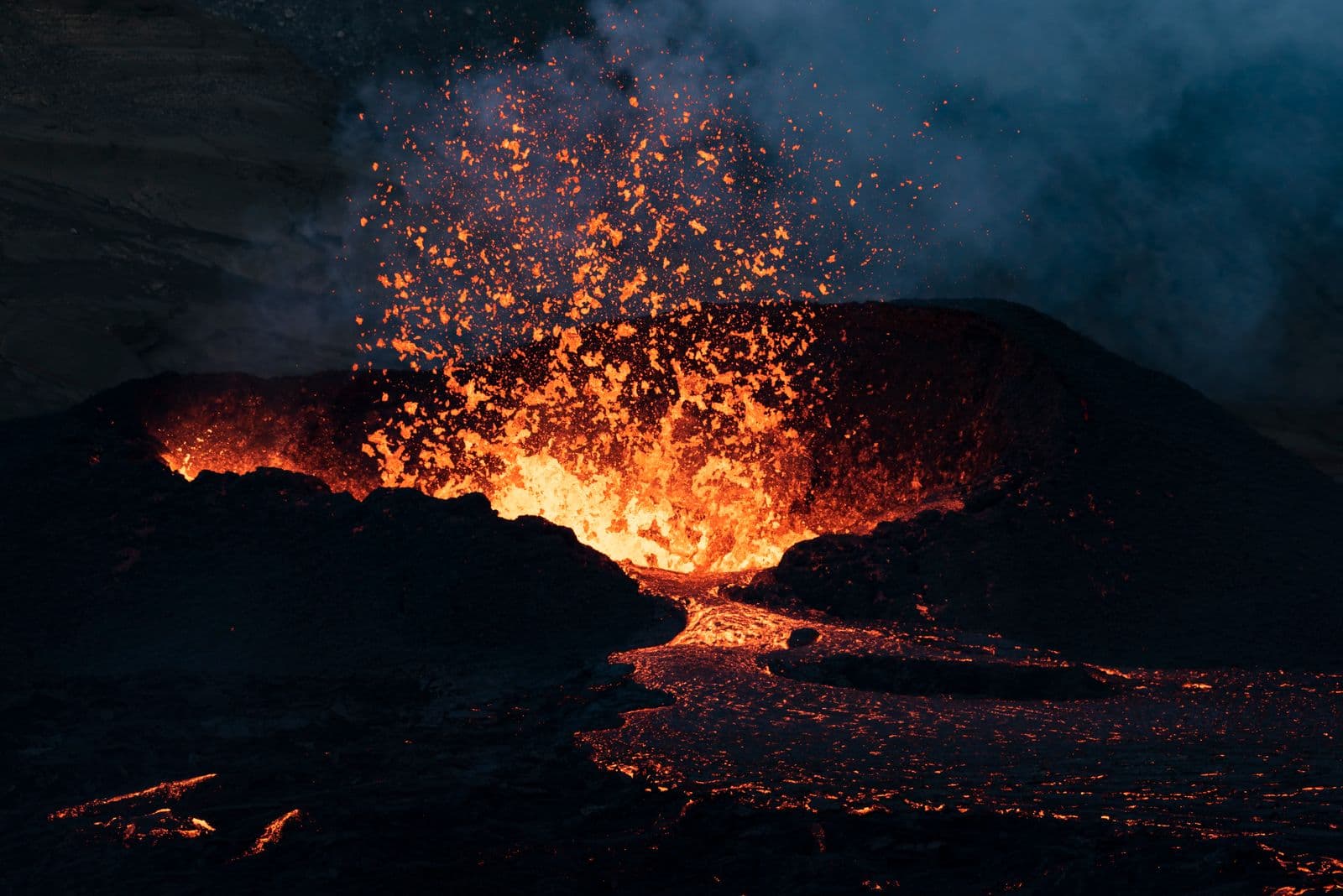 Glowing lava erupting from a vent surrounded by dark volcanic rock at night