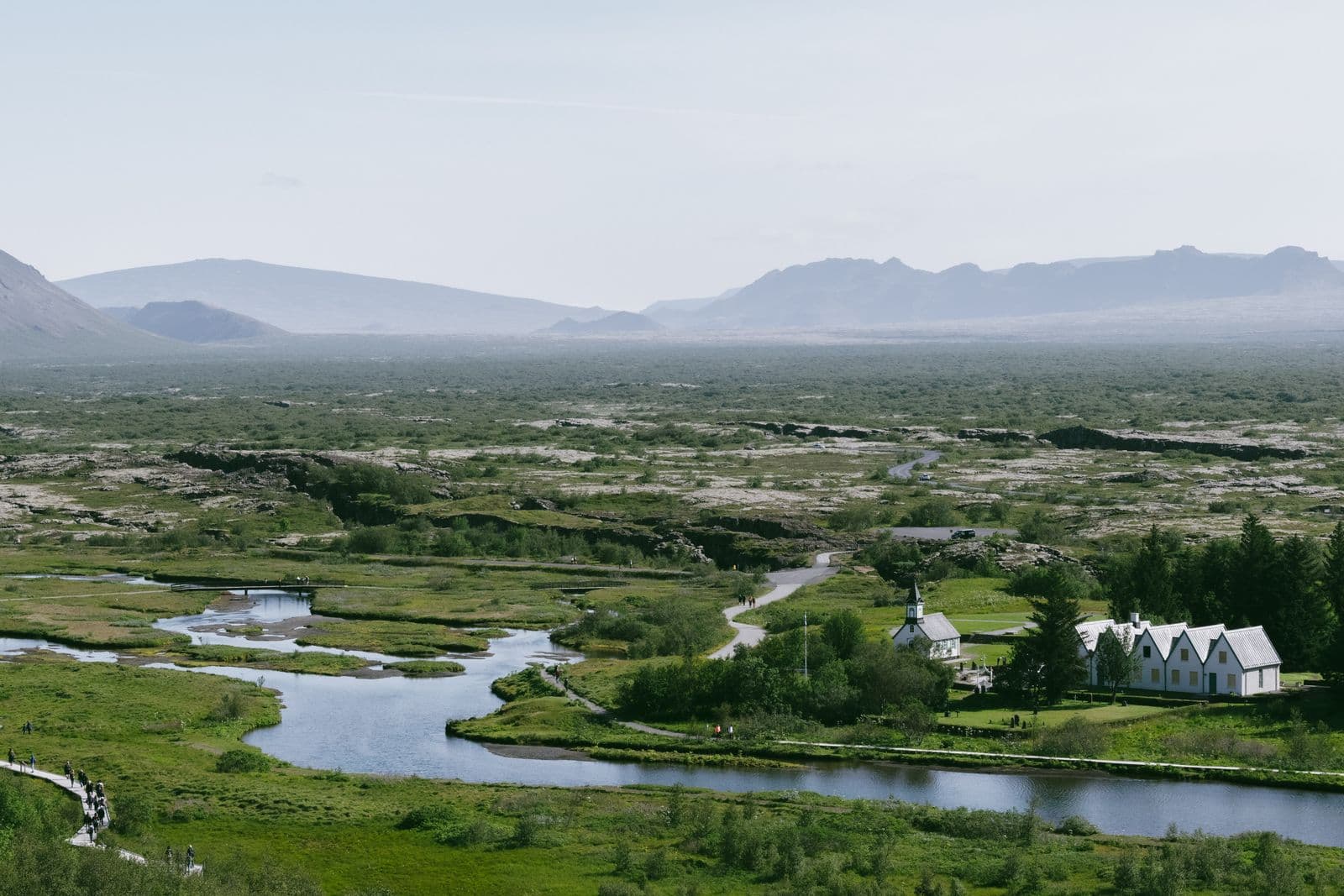 Þingvellir valley with a winding river, a small church and white farm buildings below distant mountains