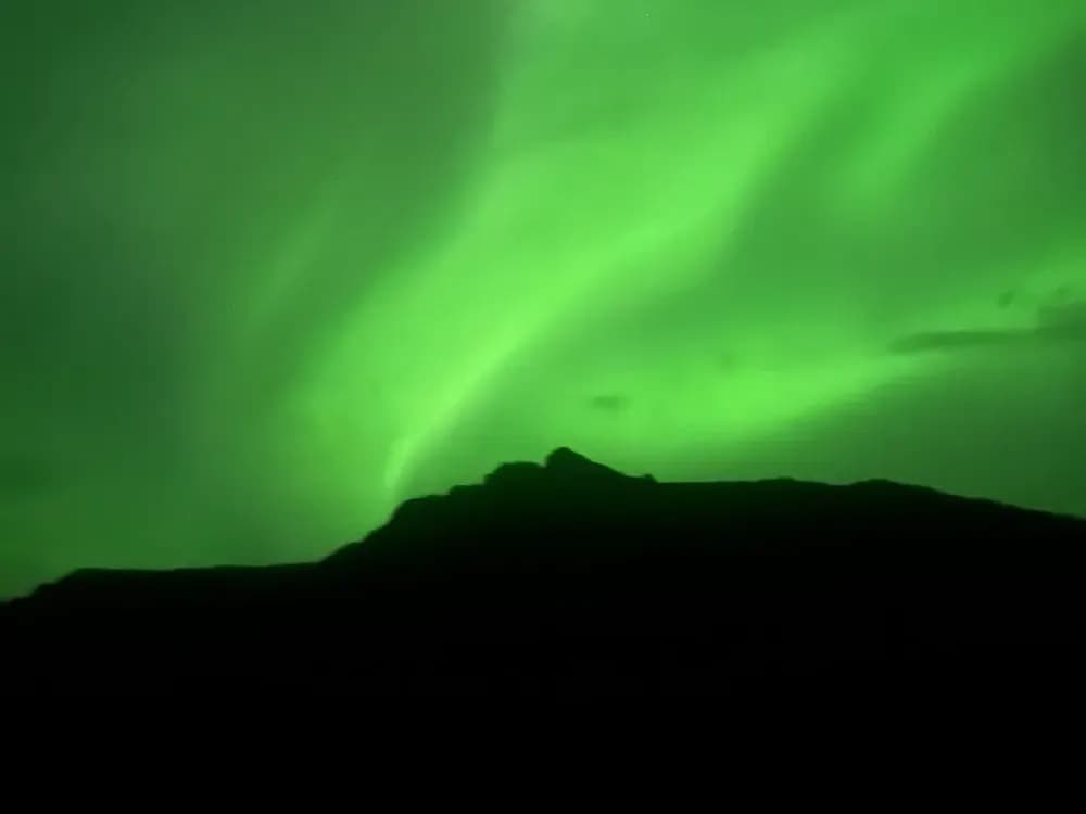 Aurora boreale verde brillante sopra una cresta montuosa scura