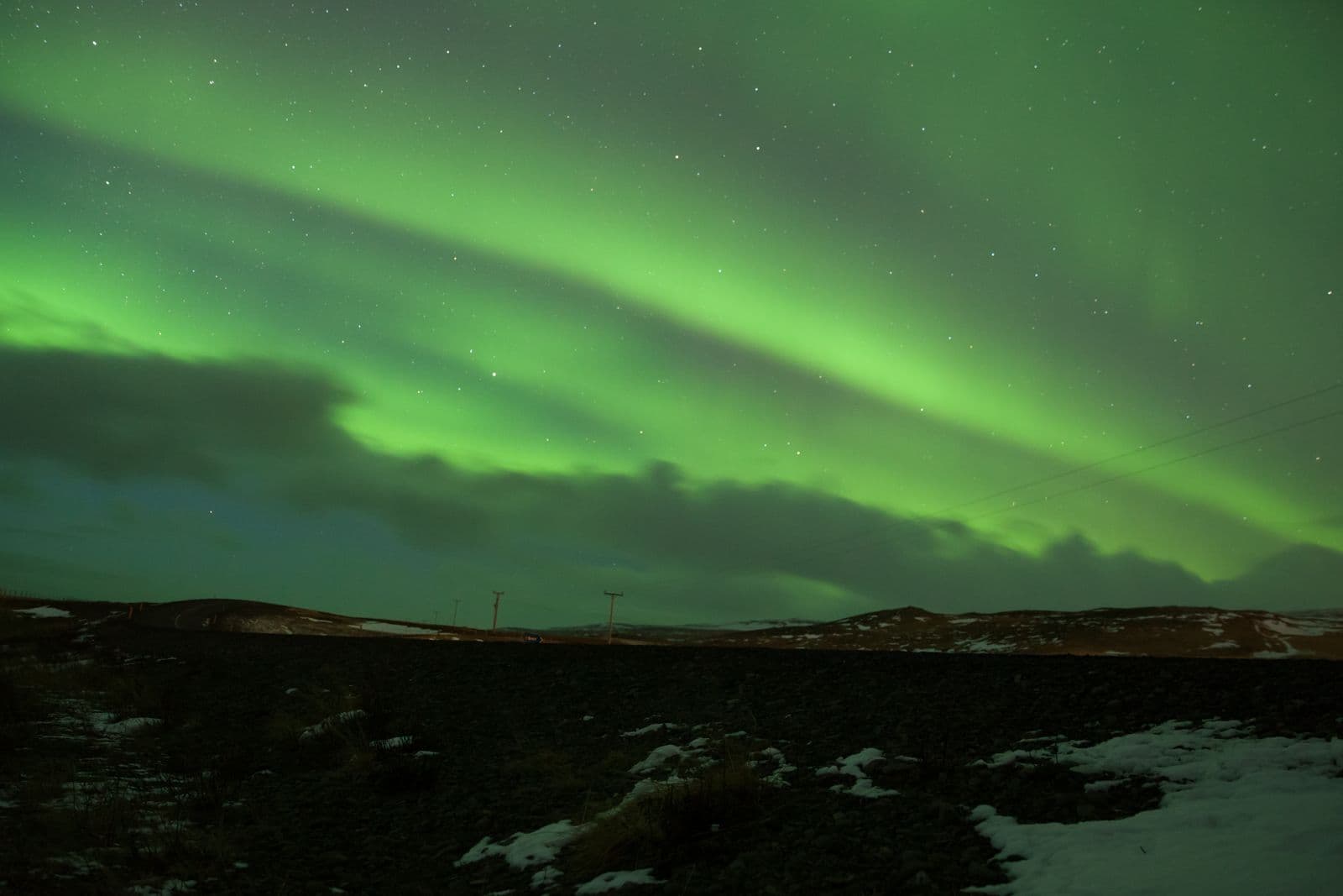 Green aurora across the sky above a dark Icelandic landscape with patches of snow