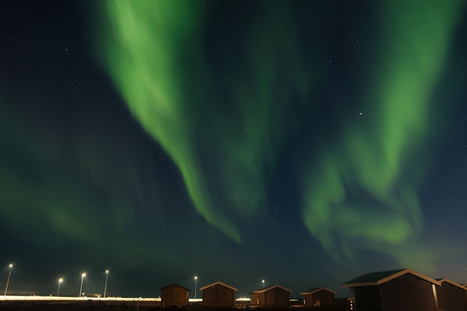Northern lights glowing green over small cabins under a starry sky in Iceland