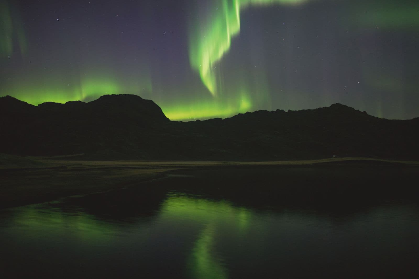Bright green aurora borealis above a dark Icelandic landscape