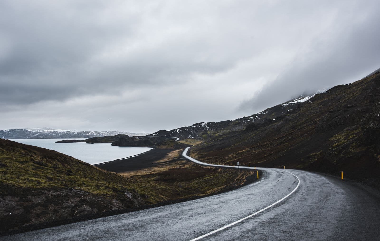 Winding road through snow-covered mountains and open fields in Iceland