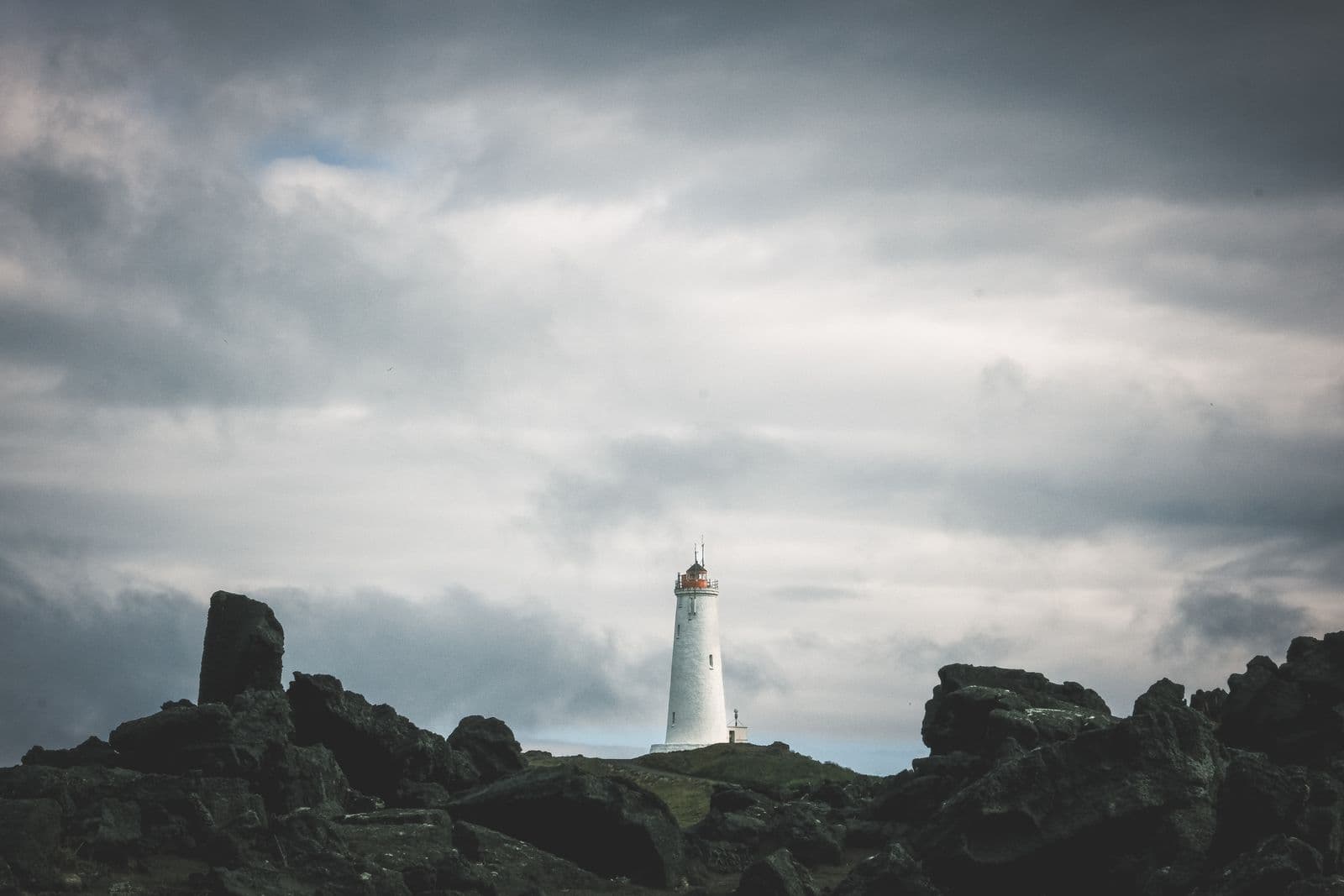 Lighthouse standing among dark lava rocks under a stormy sky on the Icelandic coast