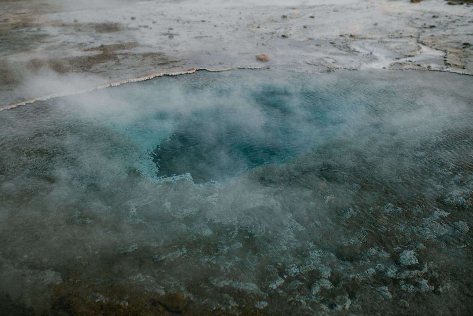 Steaming blue geothermal pool with mineral deposits at the edge in an Icelandic geothermal area
