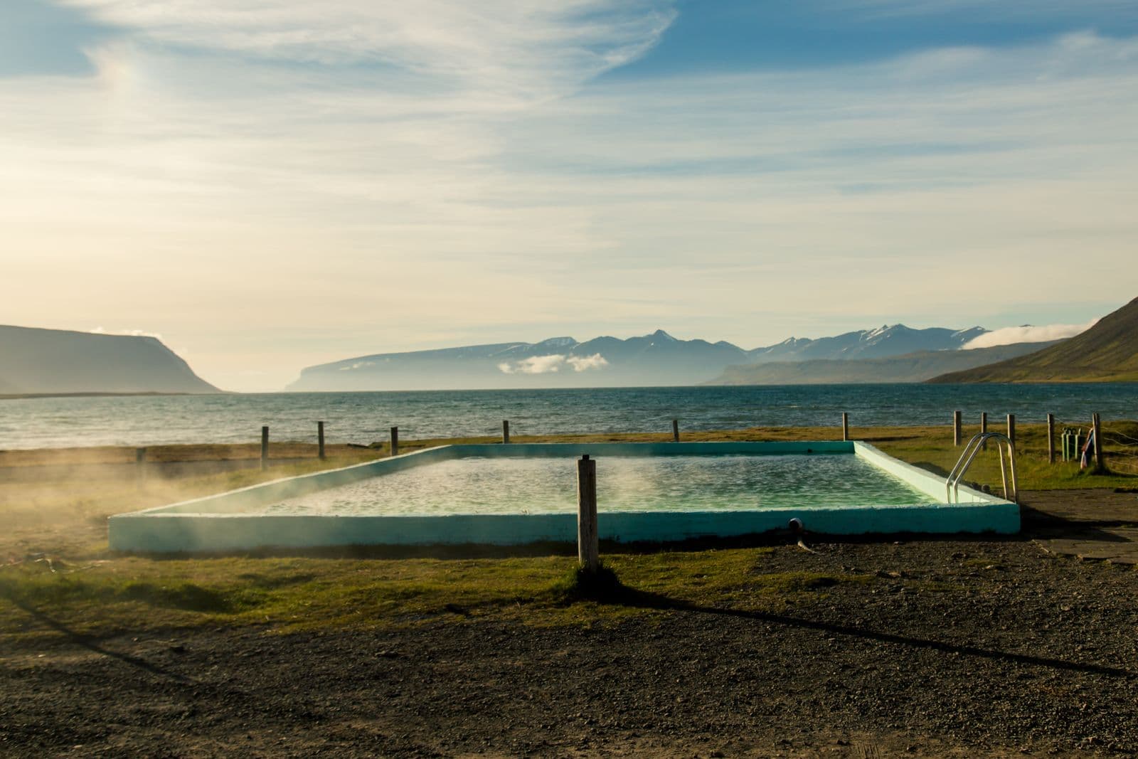 Steaming outdoor geothermal pool beside a fjord and mountains in Iceland