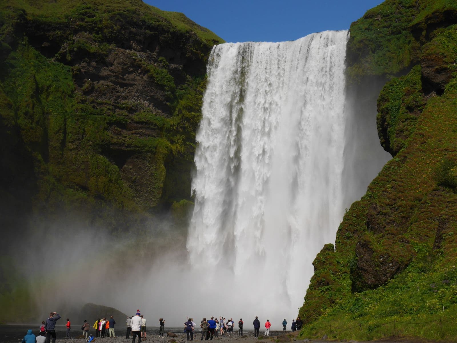 Visitors standing at the foot of Skógafoss in summer