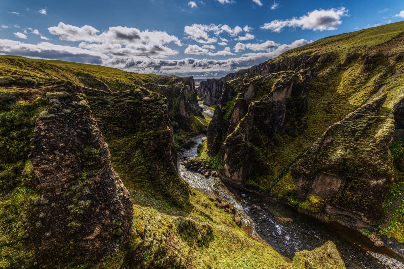Fjaðrárgljúfur canyon with moss-covered rock walls and a river winding along the bottom under a blue sky