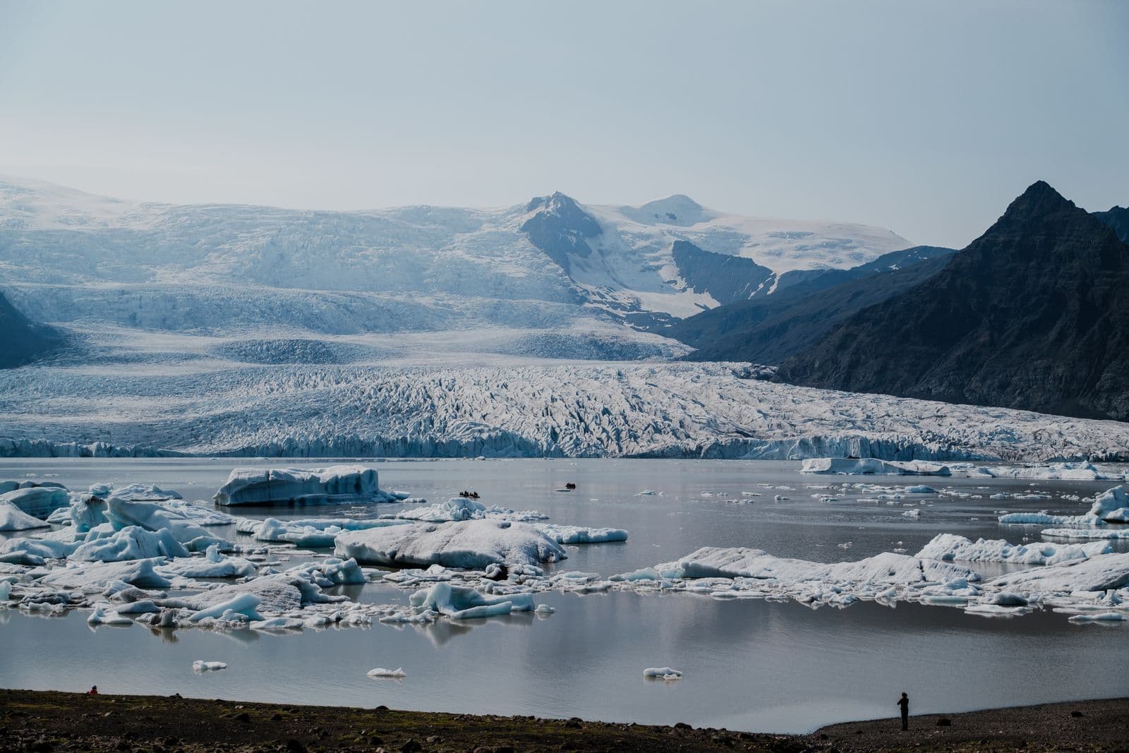 Fjallsárlón glacier lagoon with icebergs floating in front of a wide, crevassed glacier tongue and mountains