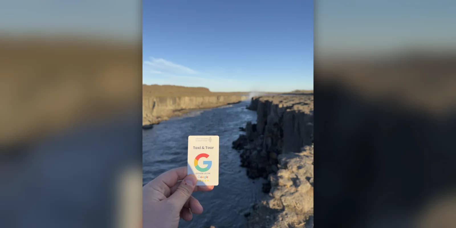 A hand holding a review card above a river canyon with basalt column cliffs near Selfoss waterfall