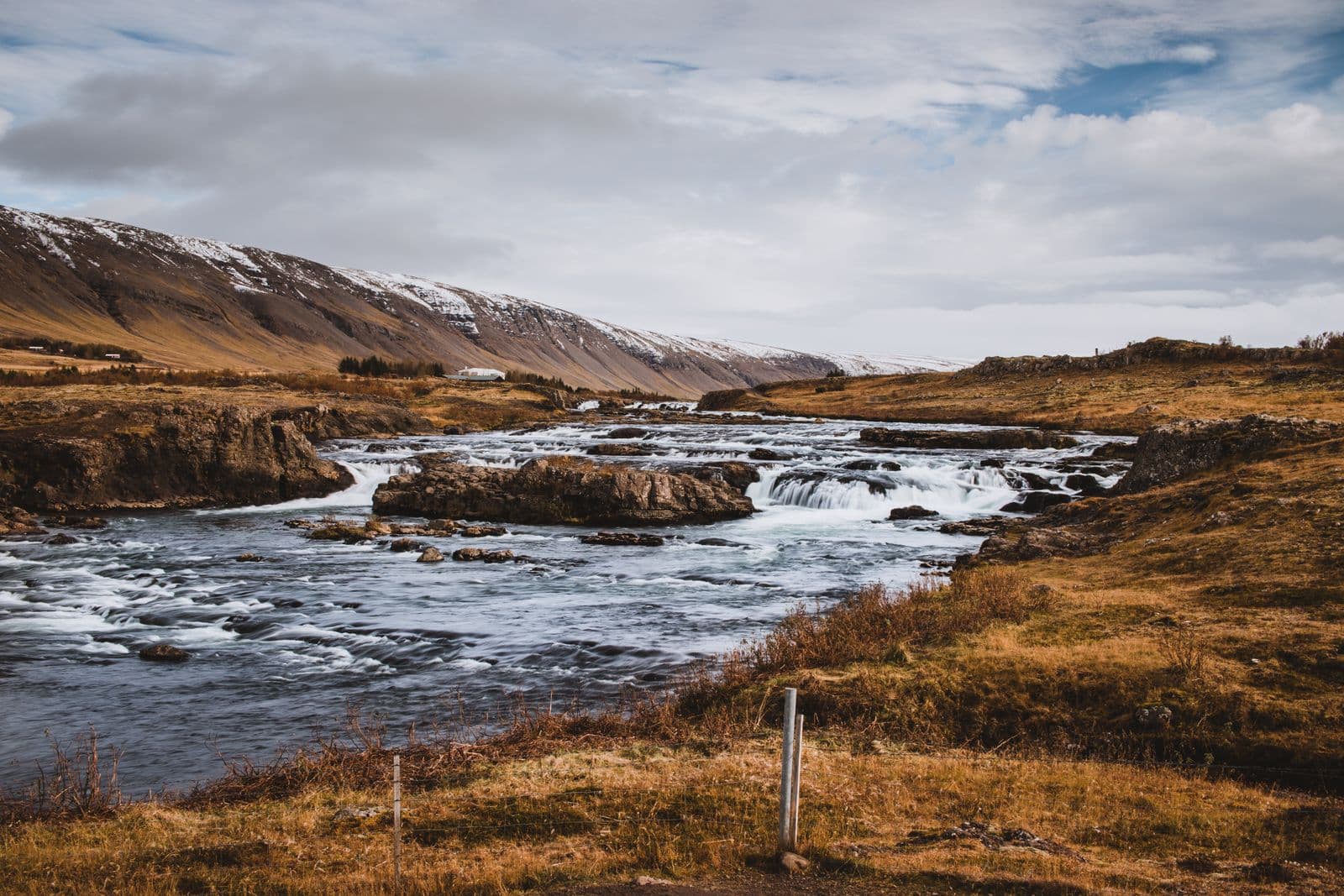 A river flowing through autumn-coloured grassland with snow-dusted mountains behind