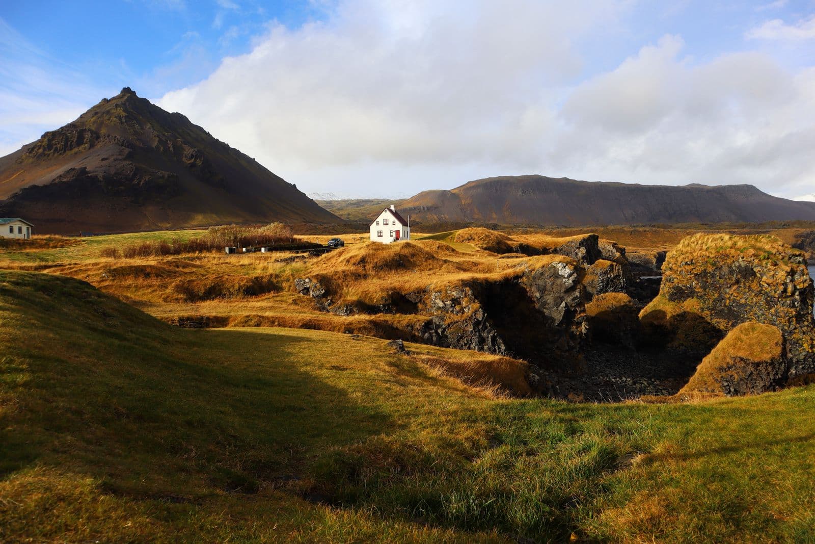 Autumn-coloured grassland and lava with a small white house below a mountain on the Snæfellsnes Peninsula
