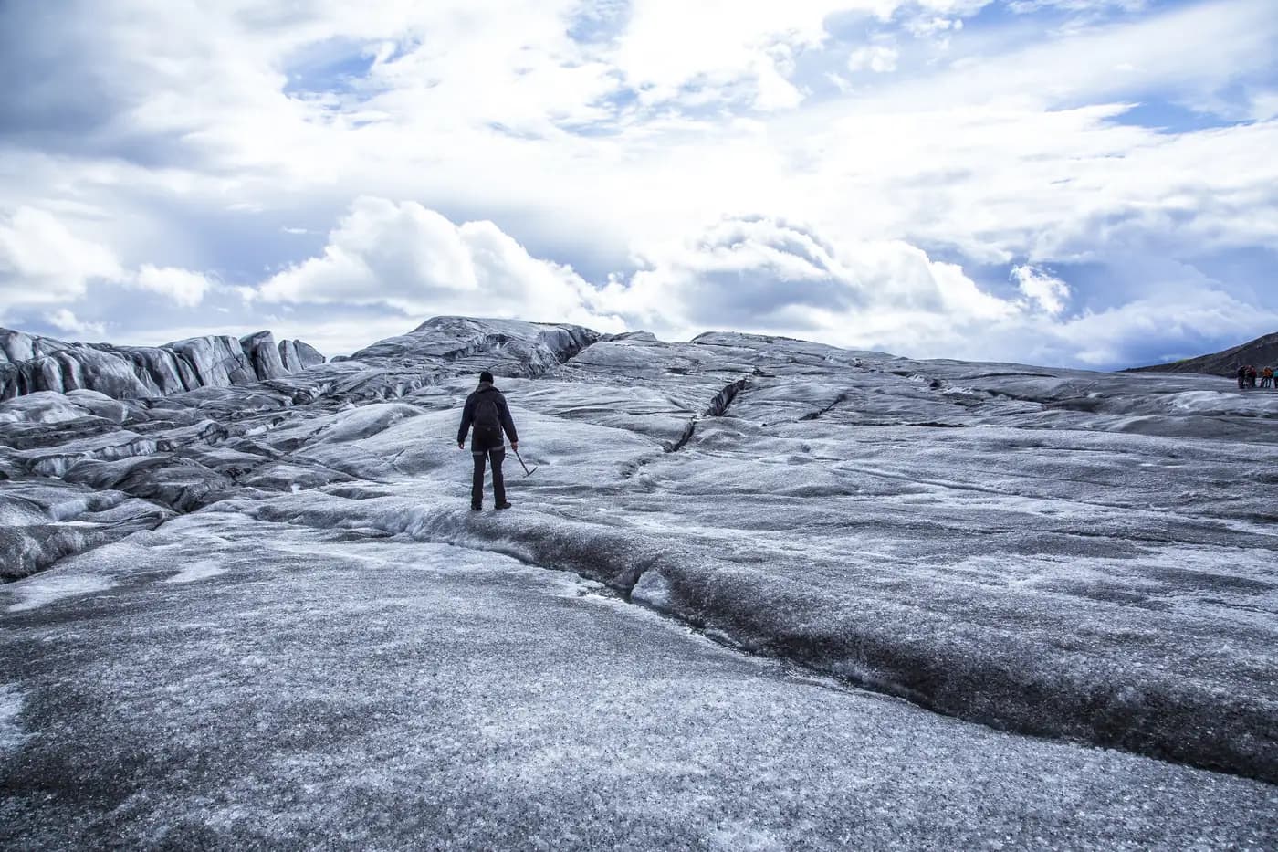 A single hiker standing on the grey and white ice of a glacier in Iceland under a dramatic sky